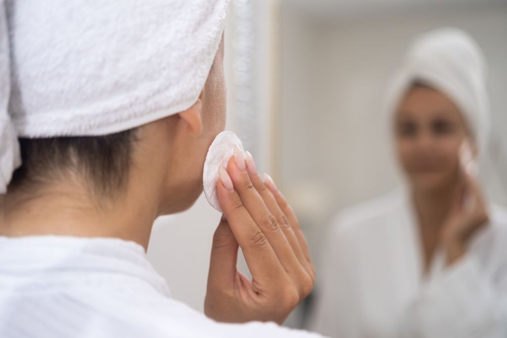  Mulher realizando a higiene facial com algodão, prática importante para prevenir o surgimento de terçol.