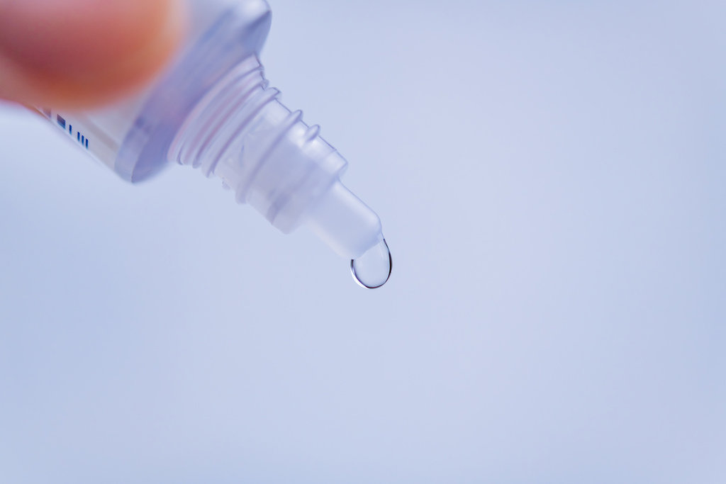 Recipiente de colírio para os olhos, com gota pendurada na abertura do pote